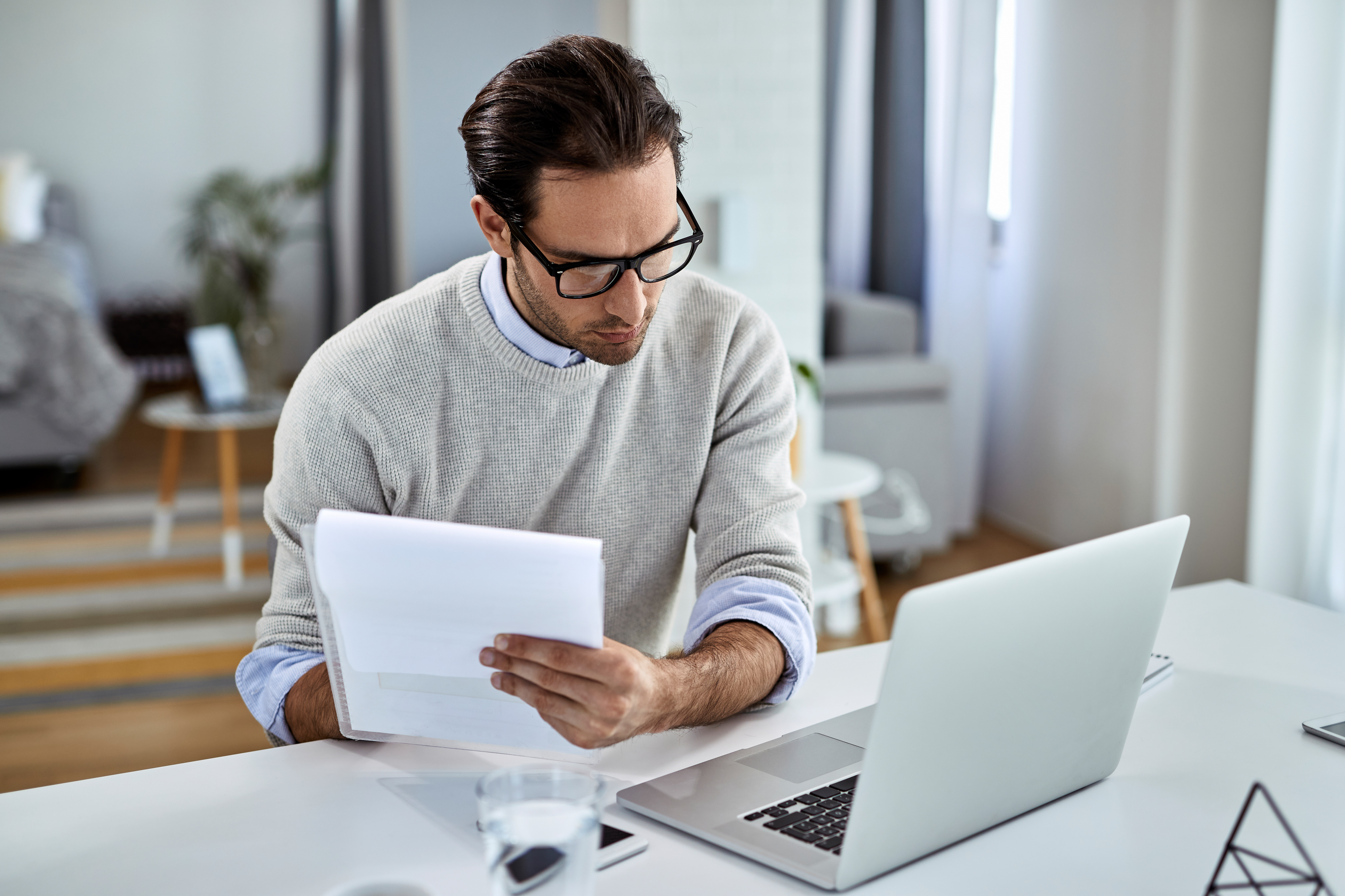 Young businessman going through paperwork and using laptop while working at home.